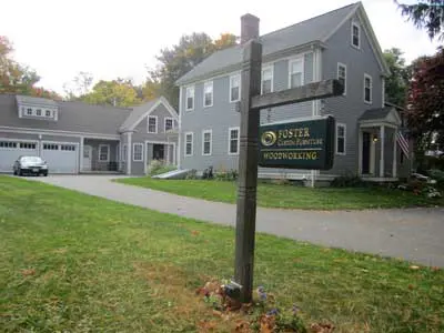 Gray house with woodworking business sign outside.