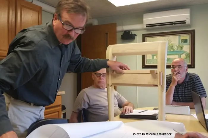 Man presenting wooden chair model to colleagues.