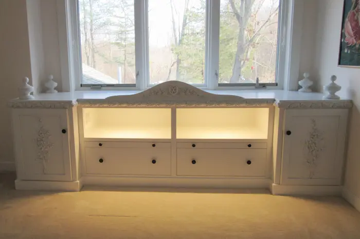 Illuminated white cabinet under large windows.