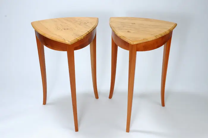 Two wooden triangular tables with curved legs.