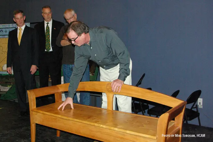 Man inspecting a wooden bench on stage.